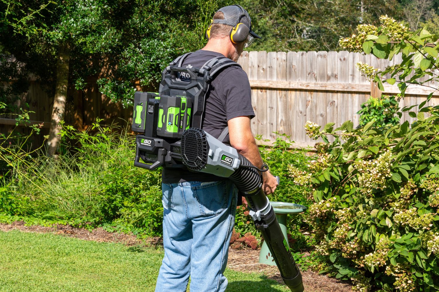 A person wearing the best backpack leaf blower option and ear protection while cleaning up the perimeter of their yard