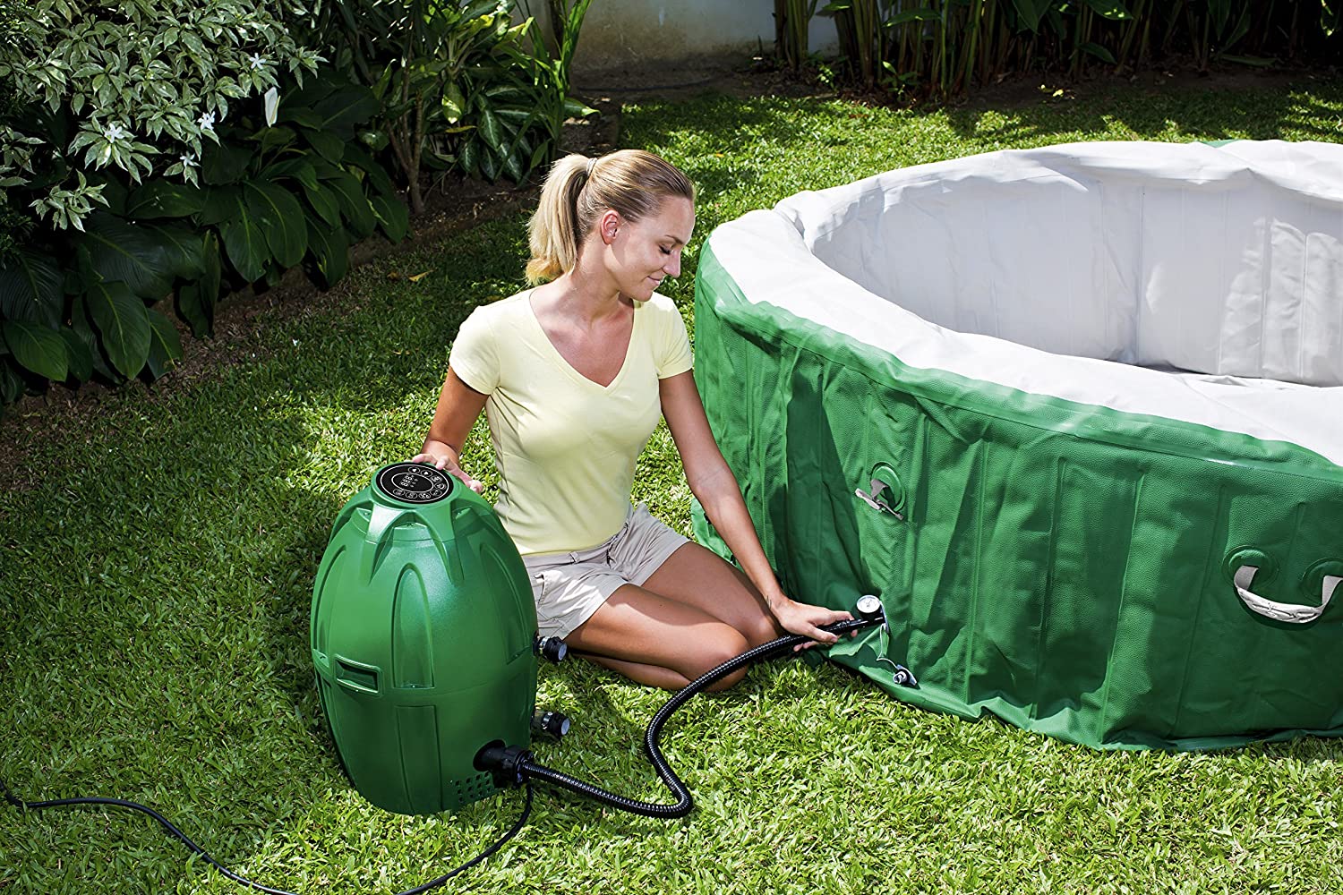 A person kneeling down in a yard while using a pump to blow up an inflatable hot tub.