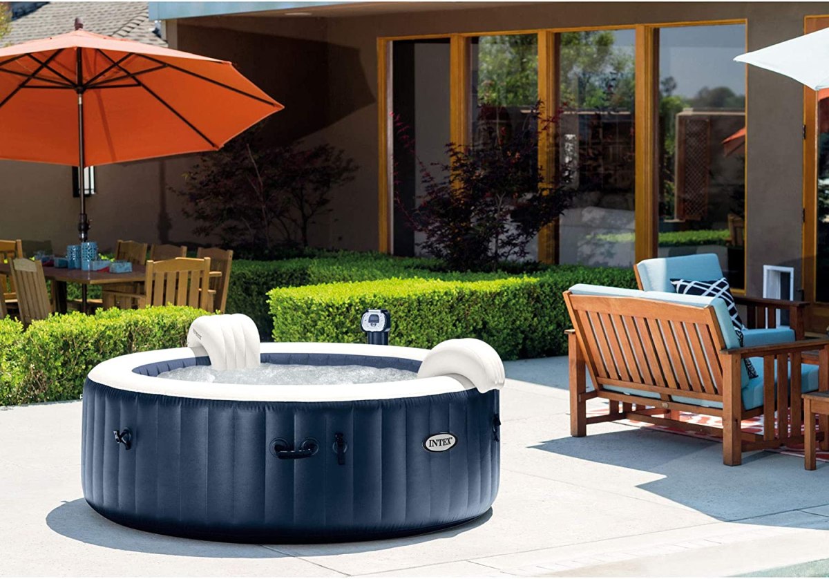 The Intex 28429E PureSpa Plus 4 Person Hot Tub set up on a cement patio next to an outdoor dining area.