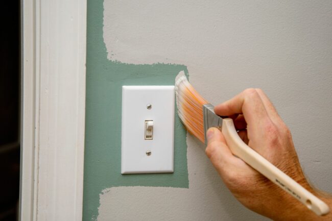 A person painting around a light switch