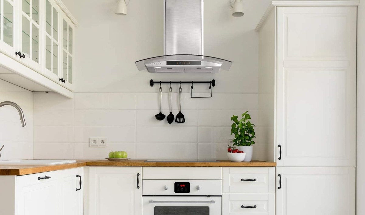 The best range hood option hangs over a white range in a clean white kitchen