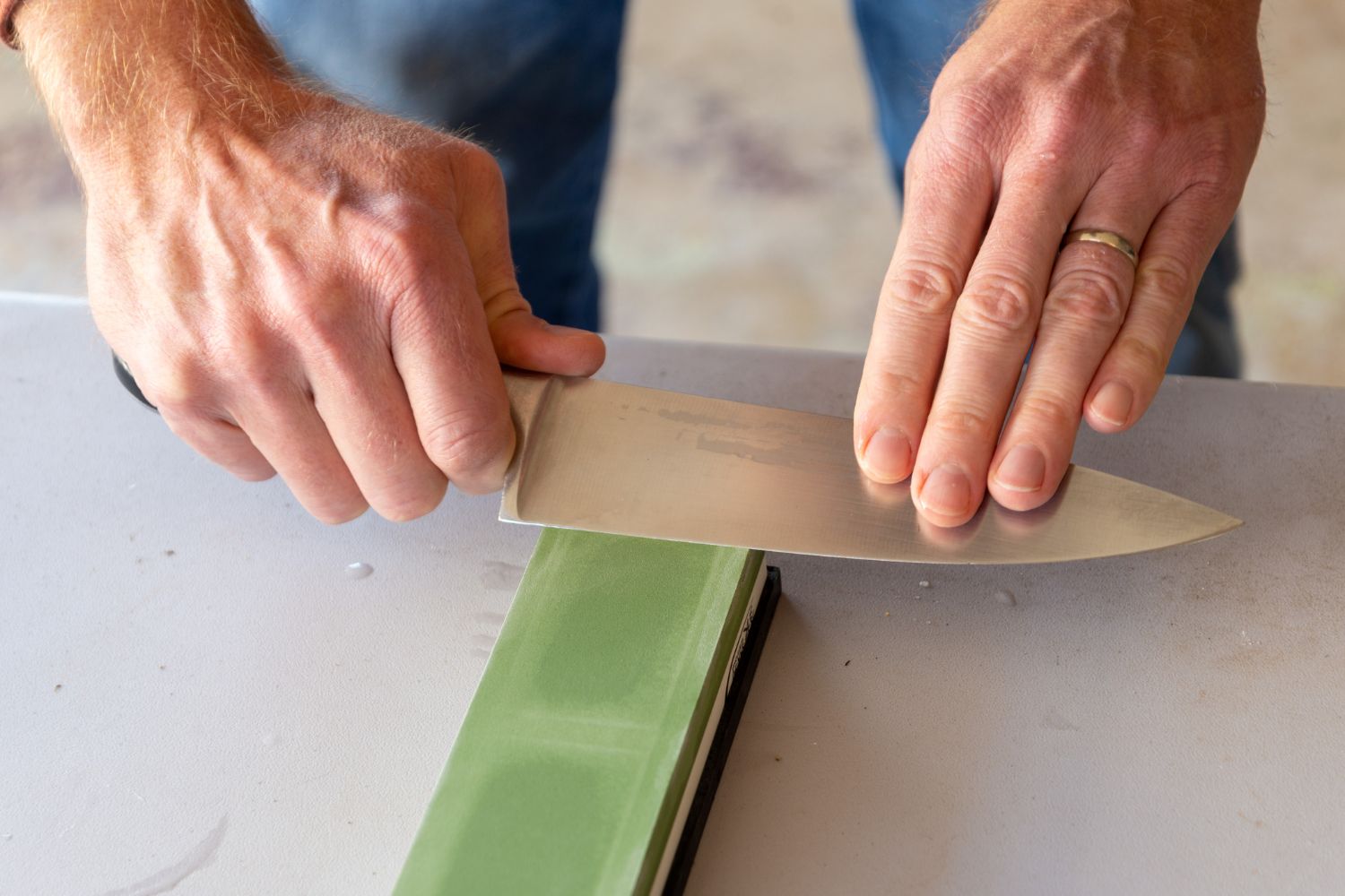 A person using the best sharpening stone option to grind the edge of a chef's knife to maintain a sharp edge.