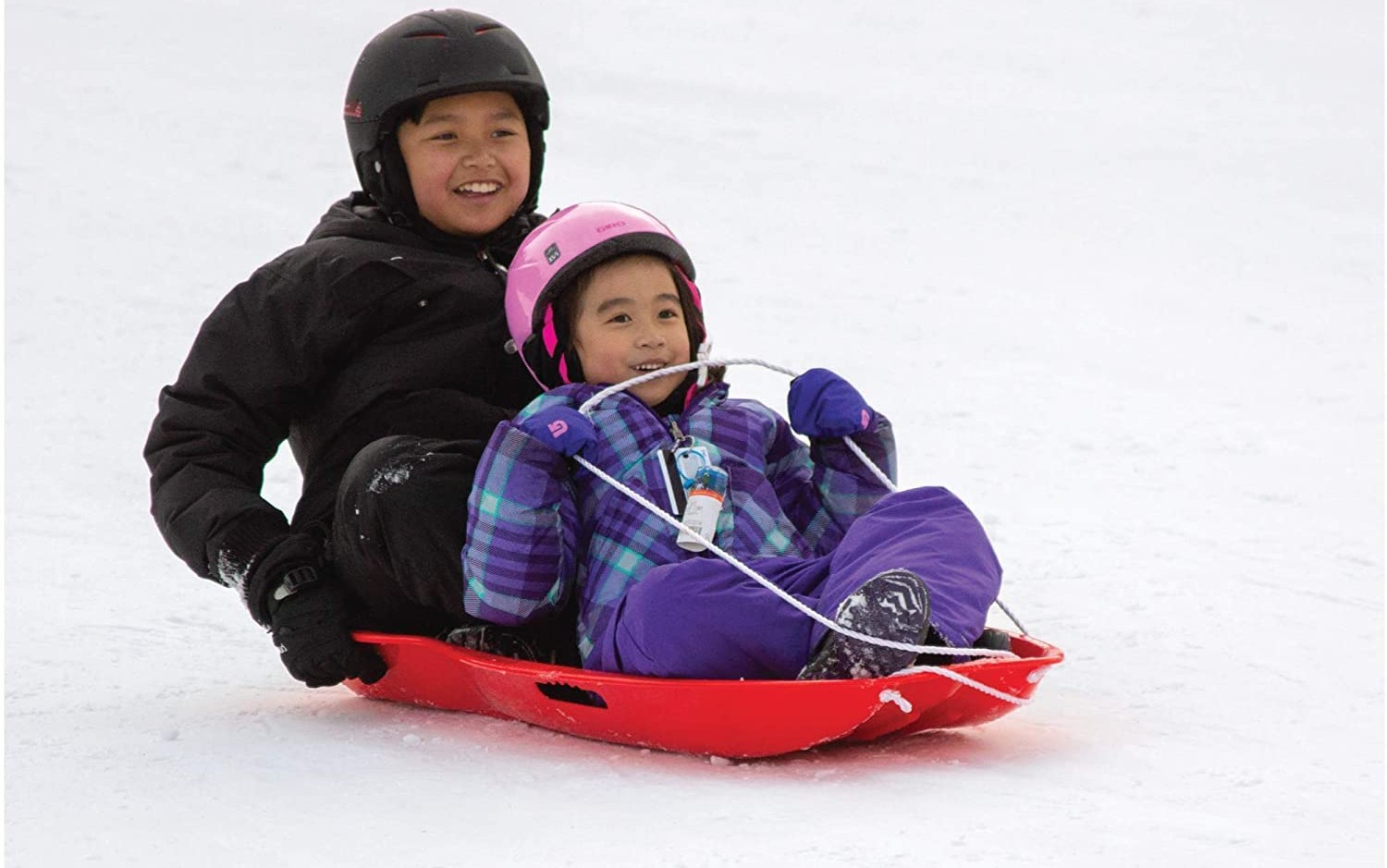 Two kids in snow gear riding together on snow in the best snow sled option.