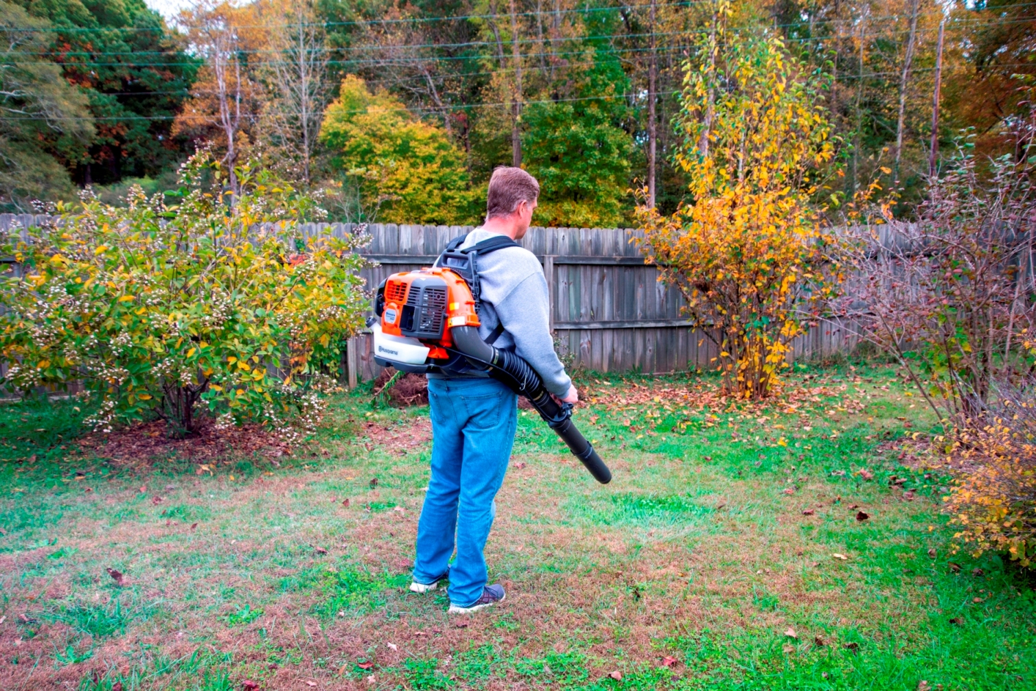 A person using an electric backpack leaf blower to do yard work in the fall.