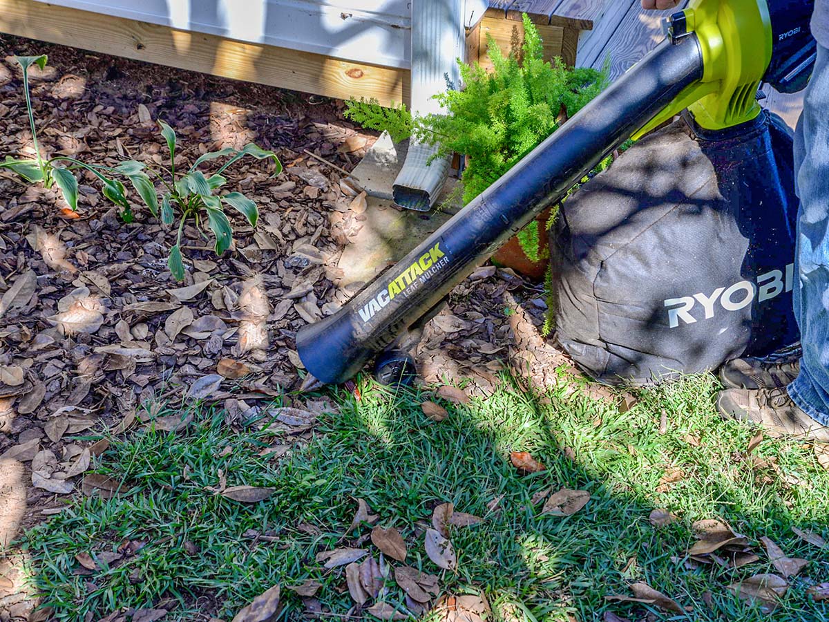 A person using the best leaf mulcher option to clear some leaves near a porch and downspout