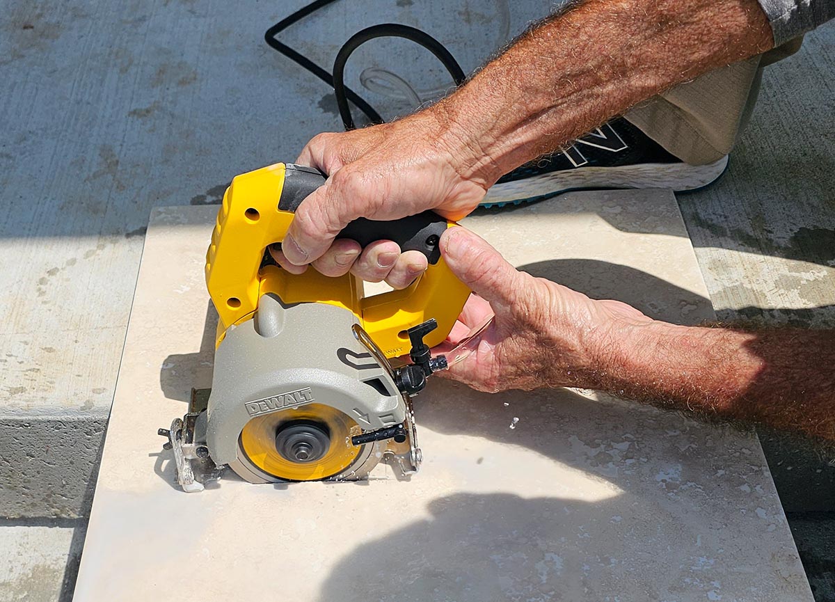 A person using a handheld version of the best tile saw option to cut a large tile