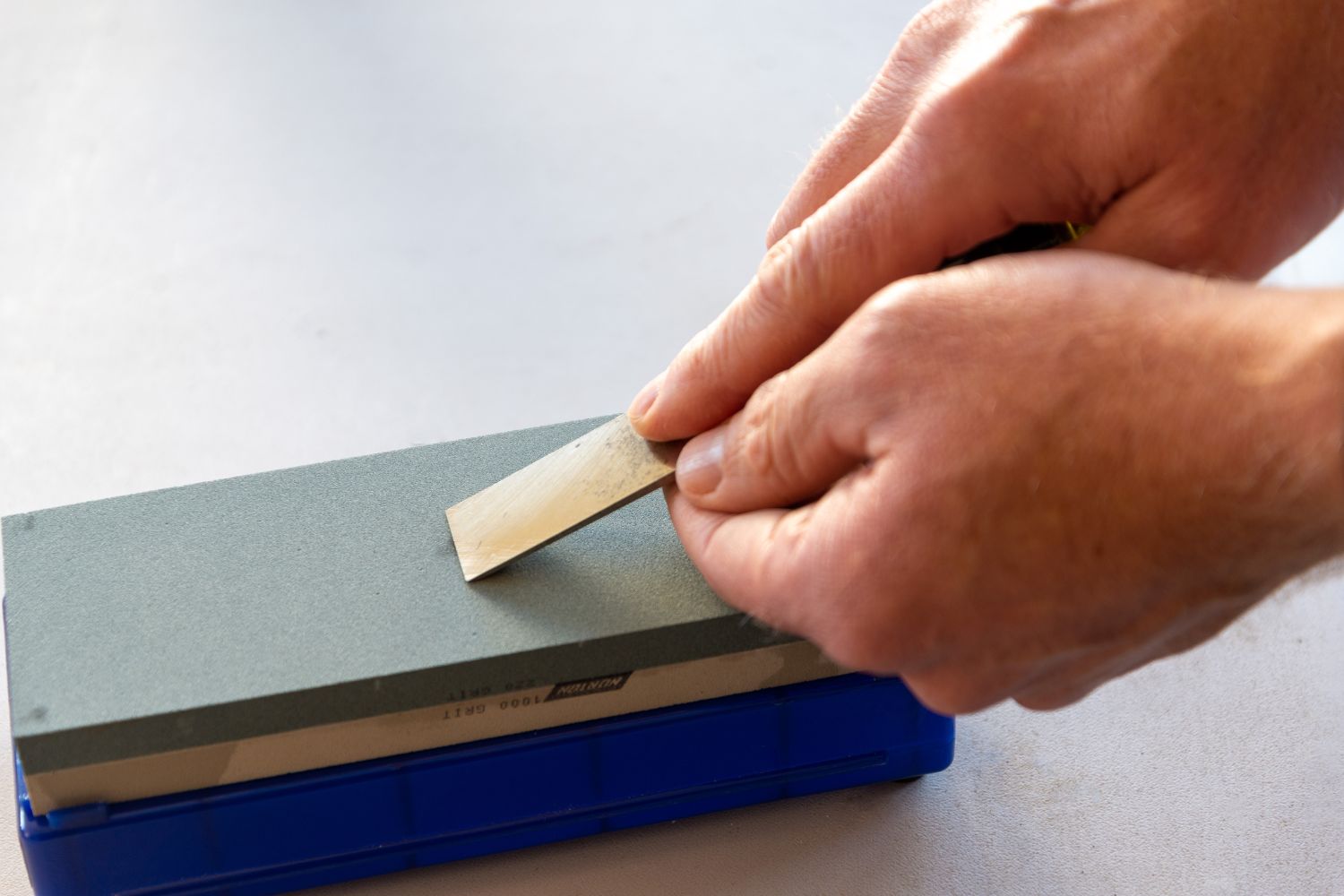 A person using the best sharpening stone option to grind the edge of small blade to maintain a sharp edge.