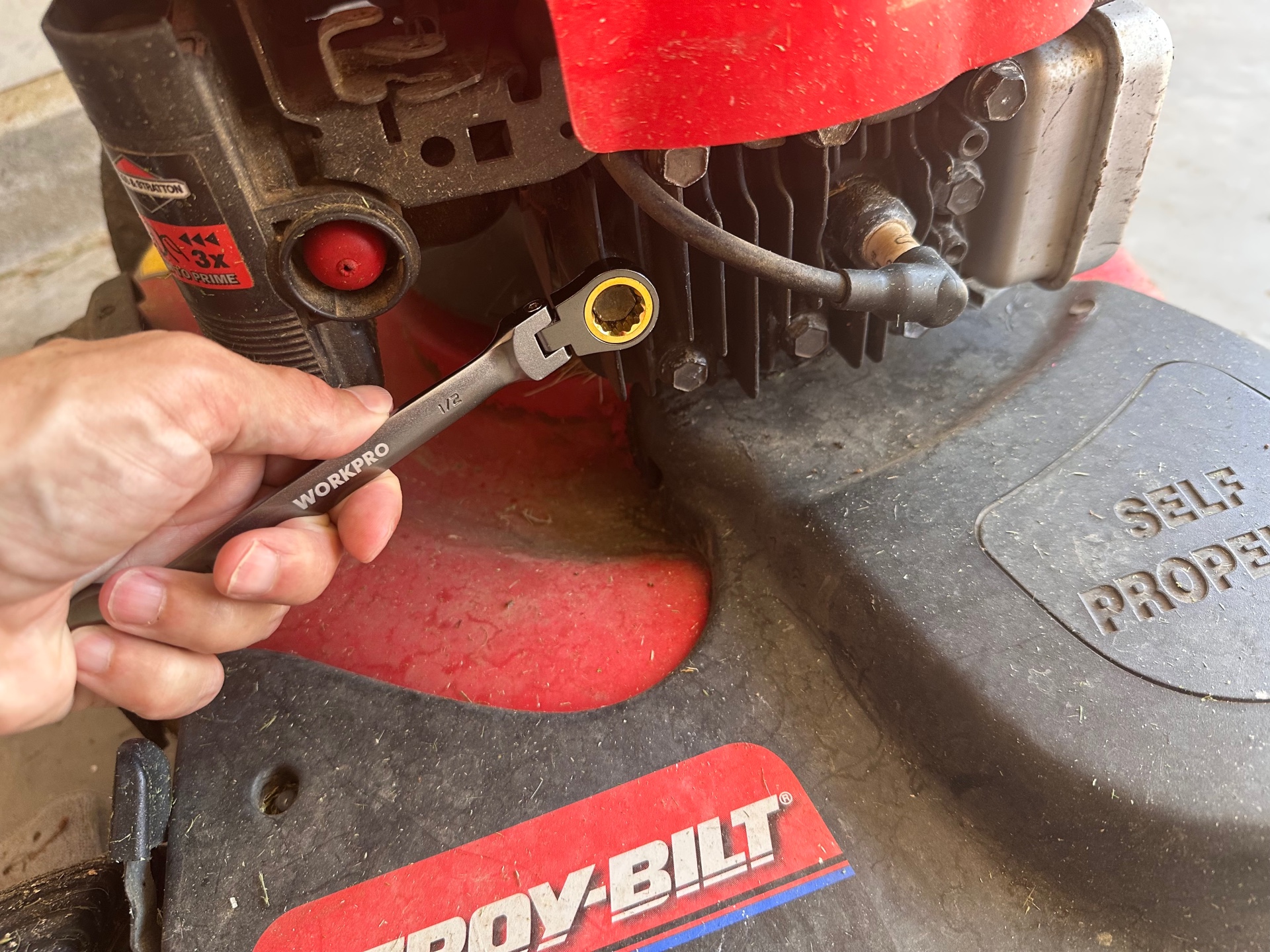 hand holding a workpro half inch ratcheting wrench near red lawn mower