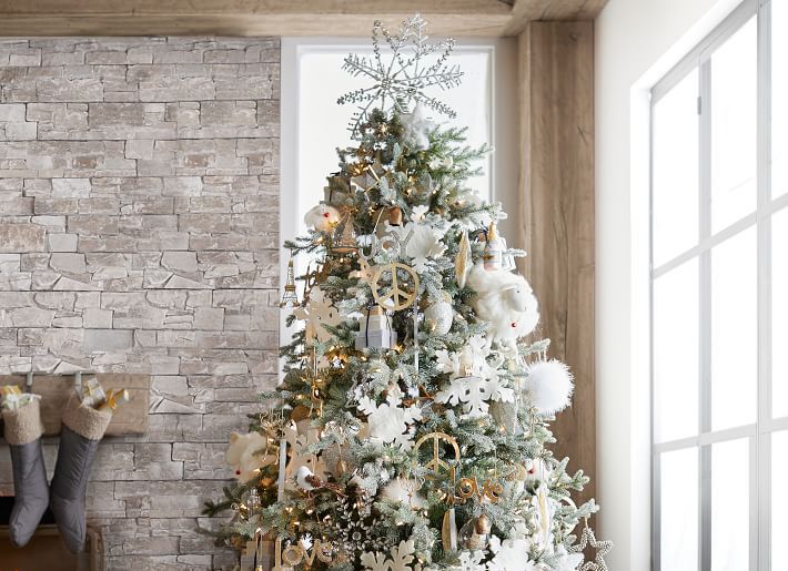 The best Christmas tree topper on a tree decorated in white, silver, and gold with a grey brick fireplace and windows in the background.