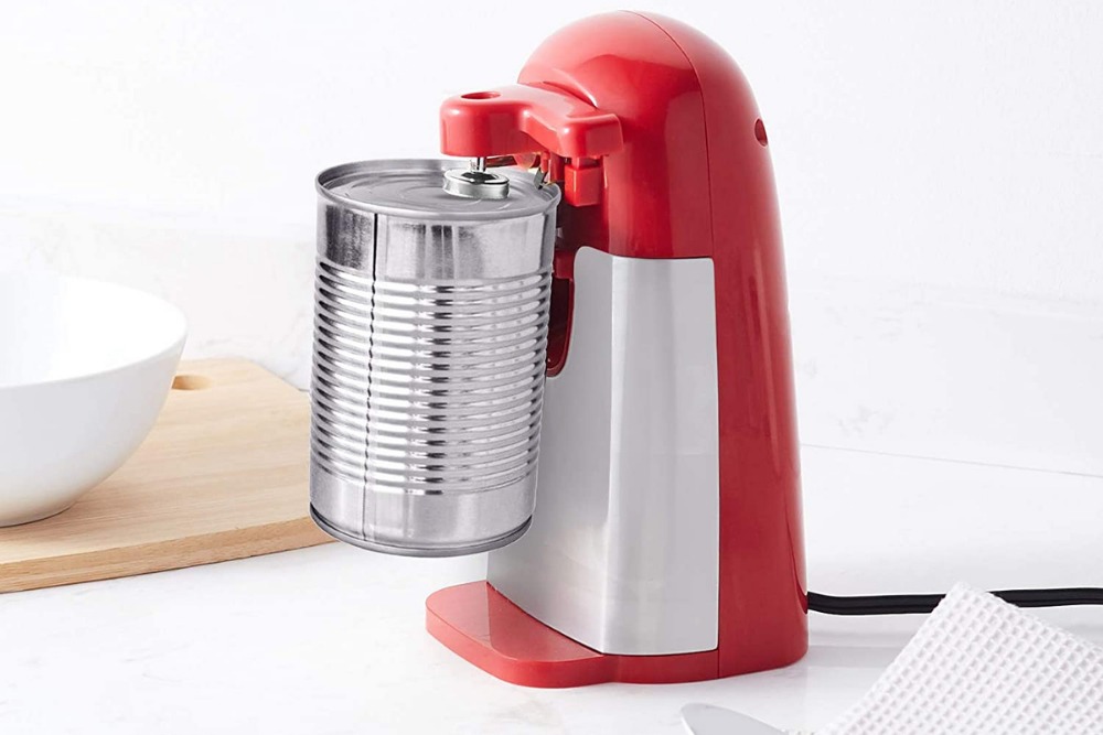 A red and white corded electric can opener on a kitchen counter with a stainless steel can of food attached prior to opening.