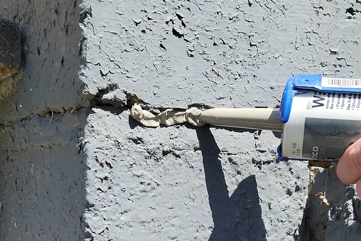 A person using the best exterior caulk to seal a crack in stucco.