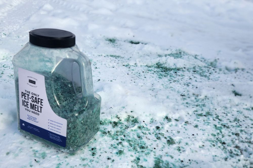 A jug of Natural Rapport The Only Pet-Safe Ice Melt You Need on a snowy and icy cement walkway.