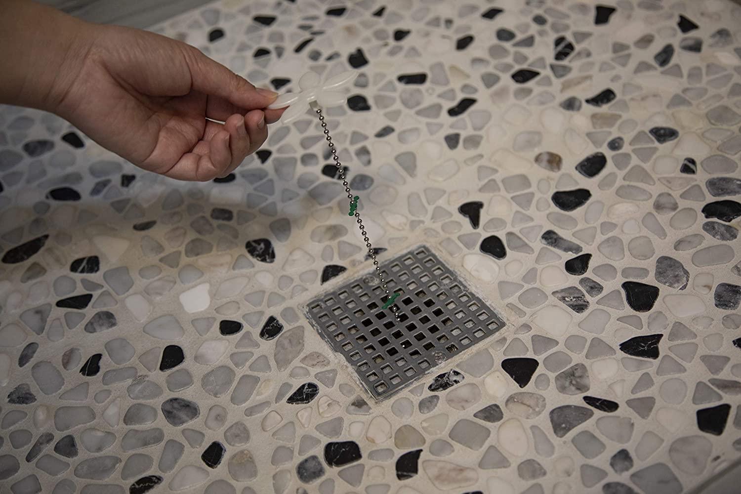 A person using the small chain on the best shower drain hair catcher option to lift it out of a shower drain