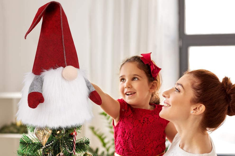A mother holding a child in her arms while putting the best tree topper on a decorated Christmas tree.