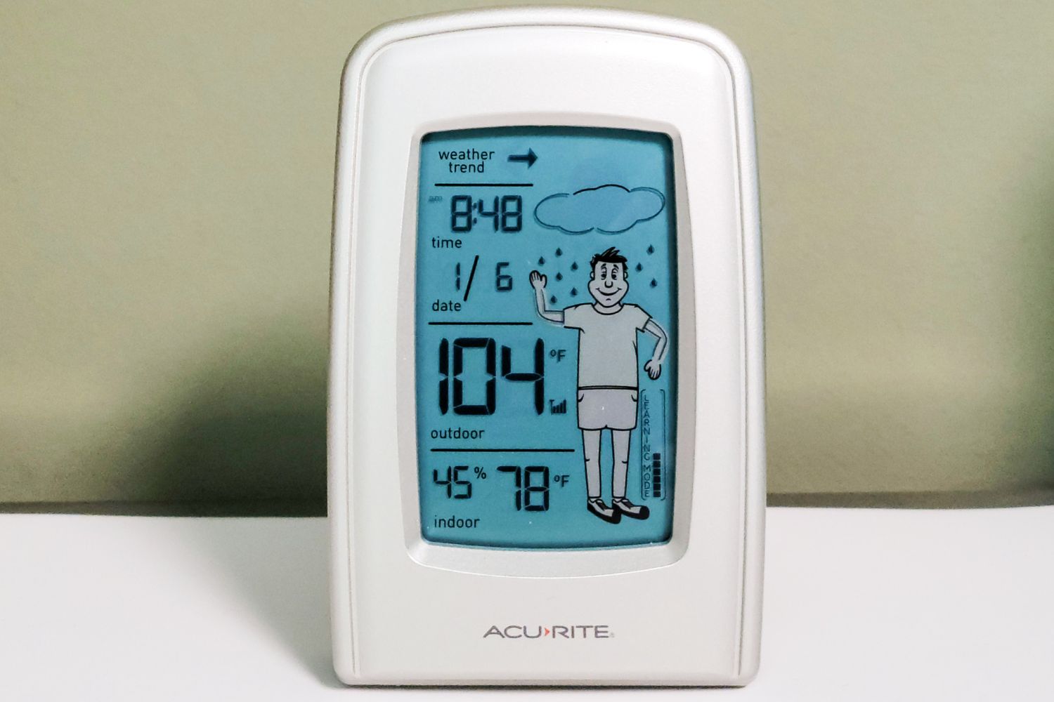 The AcuRite 00827 What-to-Wear Weather Station on a table showing a temperature of 104 degrees Fahrenheit next to an image of a boy wearing shorts.