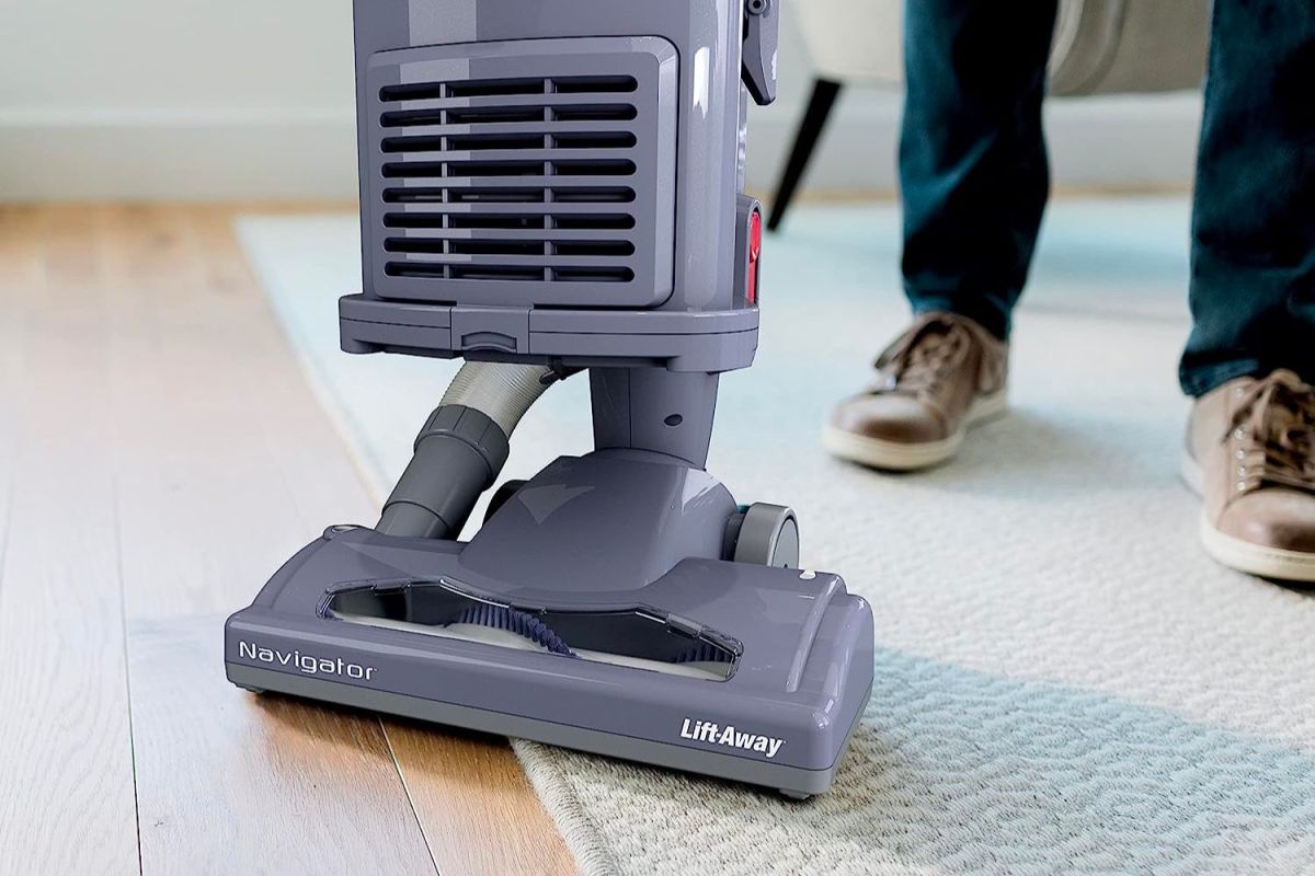 A person using the best vacuum for hardwood floors to clean the transition between a hardwood floor and an area rug.
