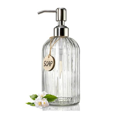 The Jasai 18-Ounce Clear Glass Soap Dispenser on a white background next to a small cluster of flowers.