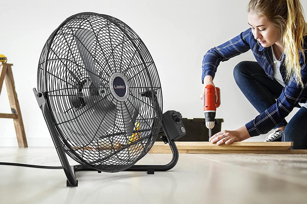 A woman drilling into the wood on the floor of a garage next to the best garage fan option