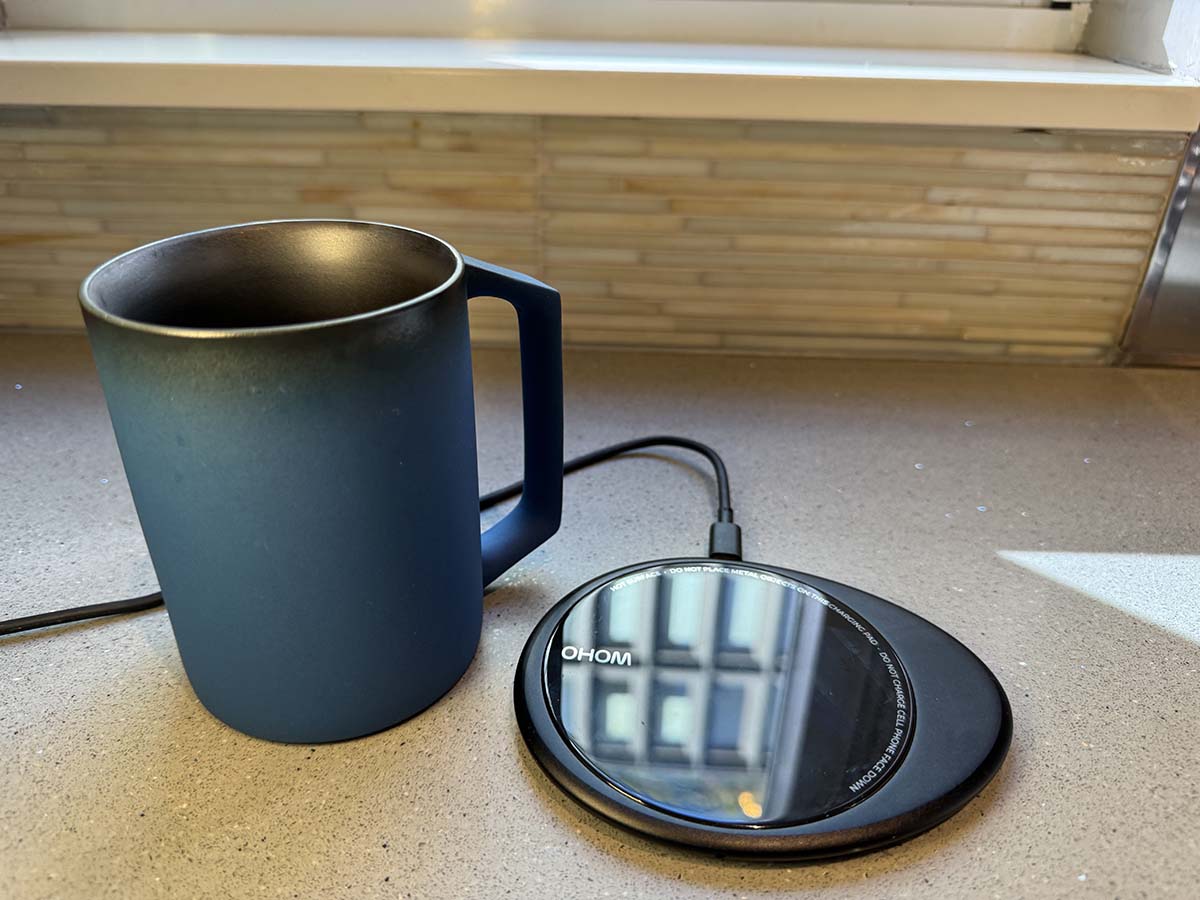 A blue Ohom Ui Artist Collection Self-Heating Mug next to its heating coaster on a kitchen counter before testing.