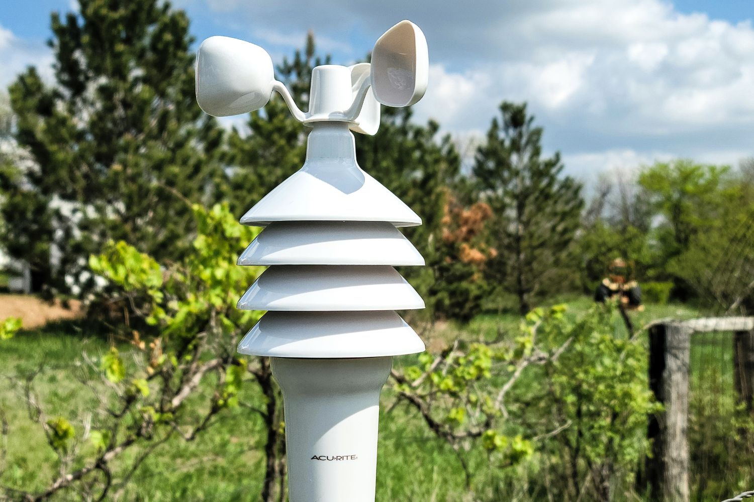 The AcuRite Notos 3-in-1 Home Weather Station and a phone showing the AcuRite installed in a lush outdoor area.