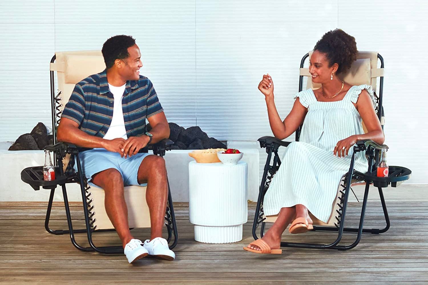 A young couple each sitting in their own best gravity chair option while outside on a deck enjoying a snack
