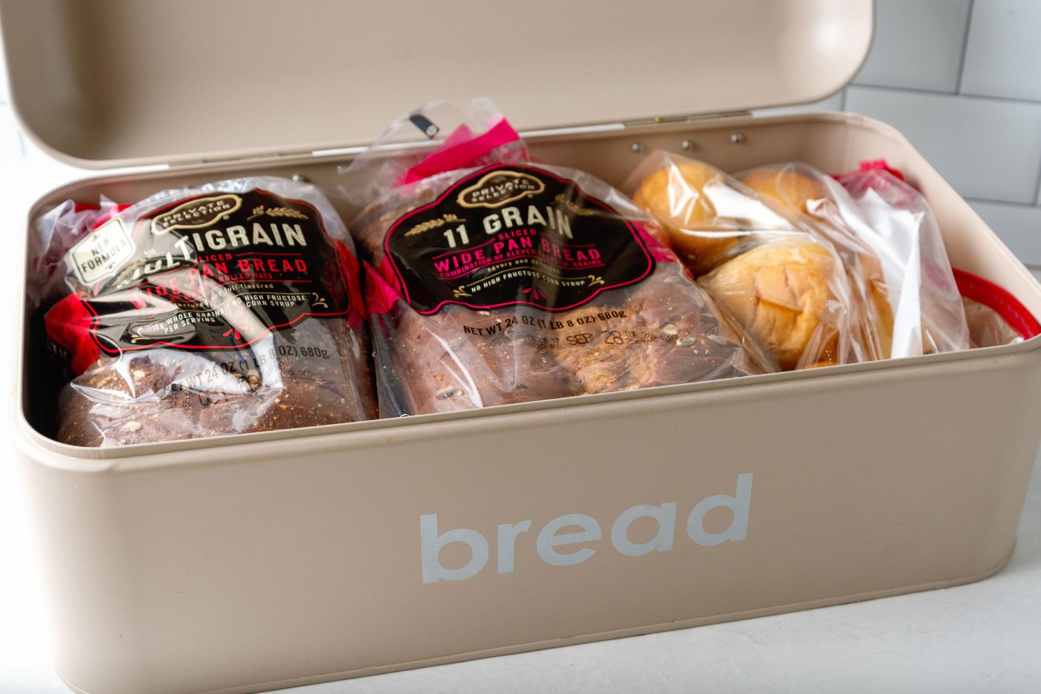 A steel bread box, ideal for keeping bread fresh, filled with sliced sandwich bread and rolls.