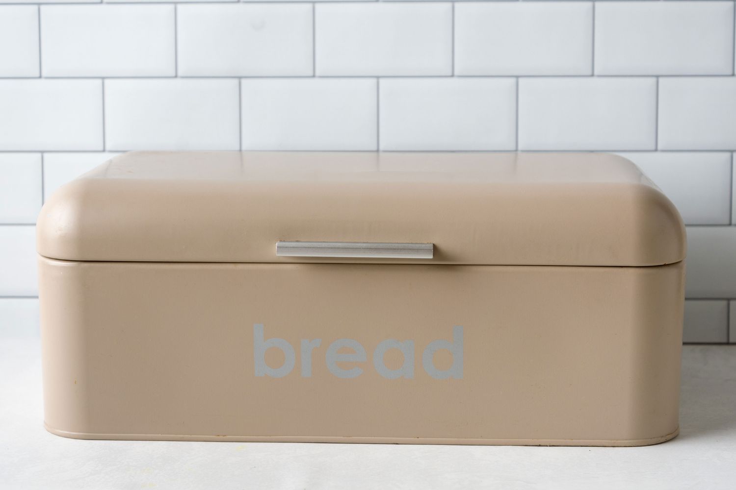A stainless steel bread box with open-close functionality on a kitchen counter in front of a tiled backsplash.