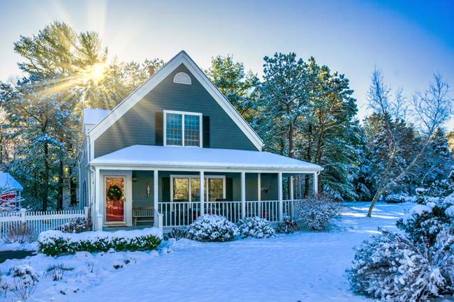 A gray home with a front porch and shutters on a sunny, snowy winter day.