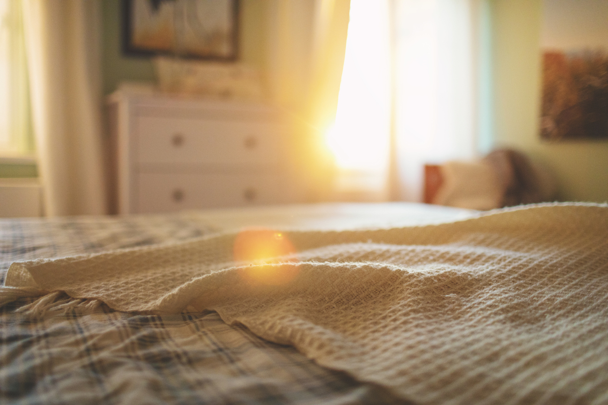 Bedroom with a bed in the foreground and sunlight streaming through the window.