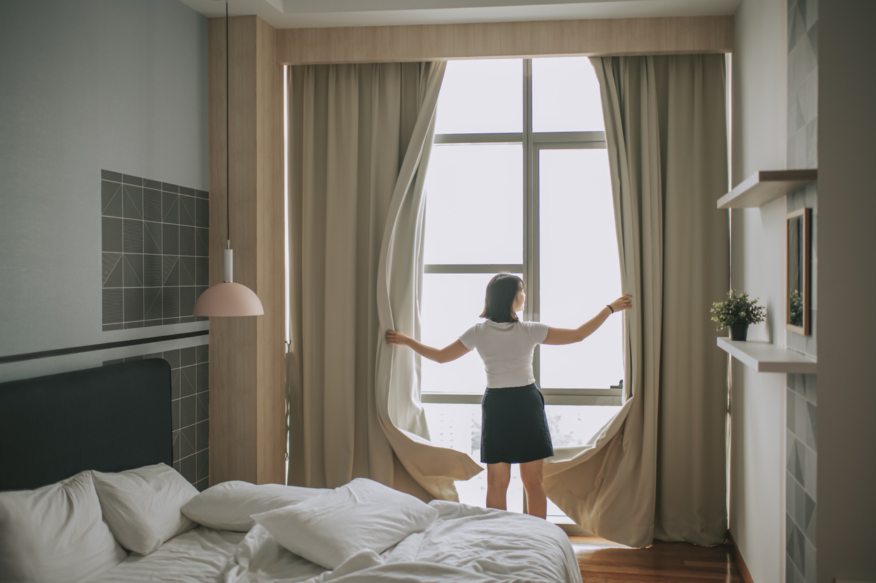 woman opening thick curtains in bedroom letting in morning light
