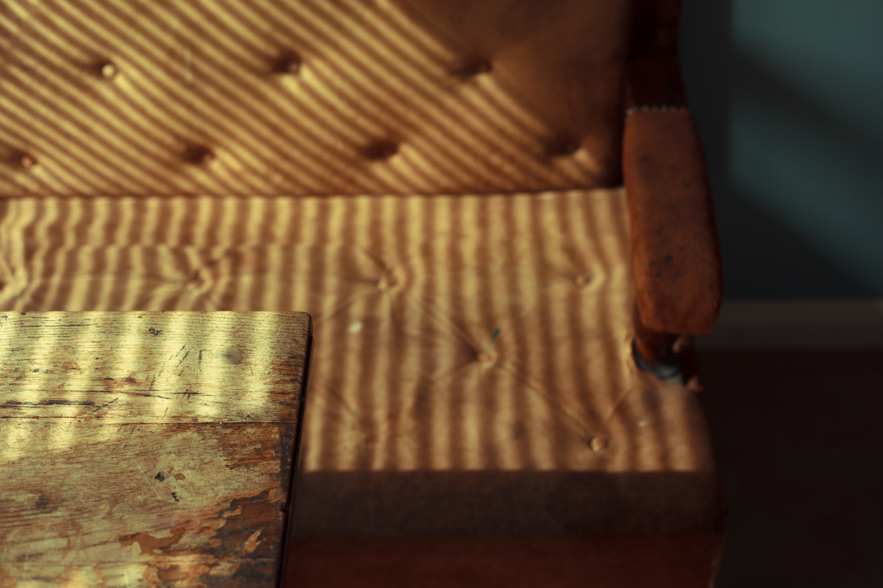 Sunlight falling onto faded brown leather couch and a wooden coffee table.