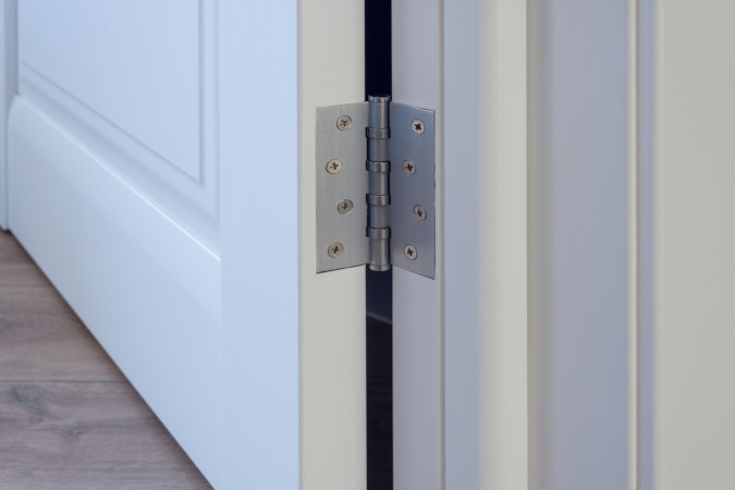 Metal door hinges on white wood door.