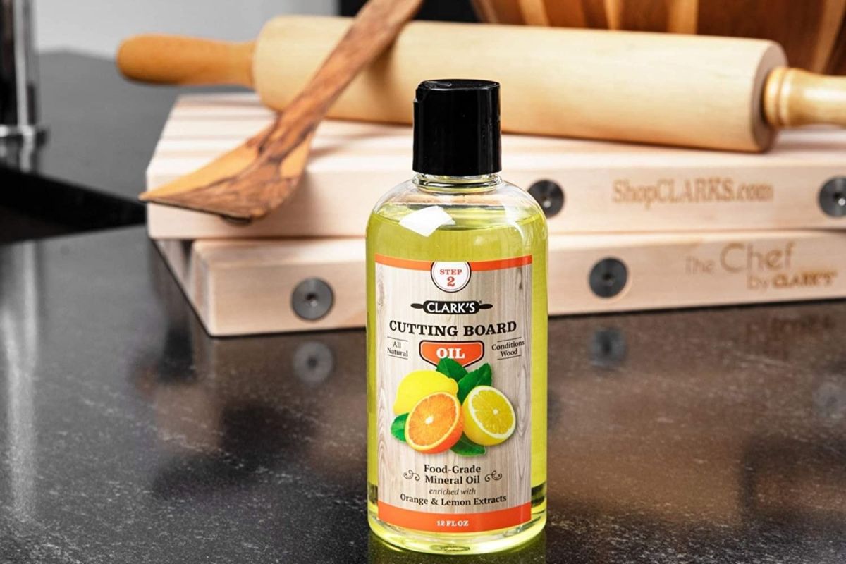 A bottle of the best cutting board oil, Clark's Cutting Board Oil, on a dark kitchen counter with two cutting boards in the background.