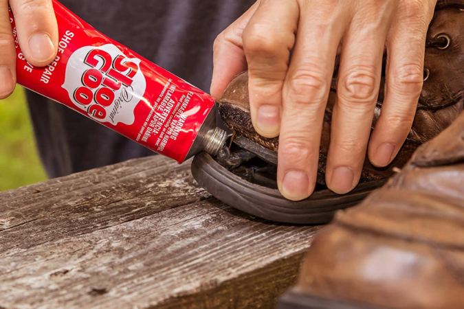 A person using shoe goo repair and protective coating to reattach a sole to a shoe.