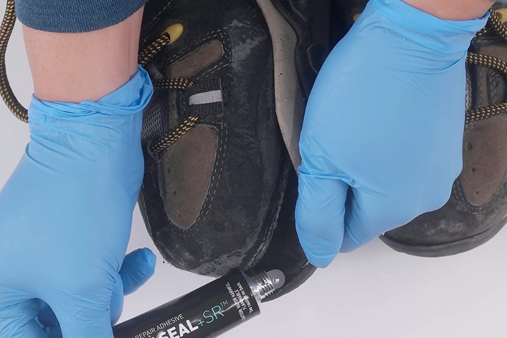A person using Gear Aid AquaSeal SR Shoe Repair Adhesive to reattach a sole to a show white wearing latex gloves.