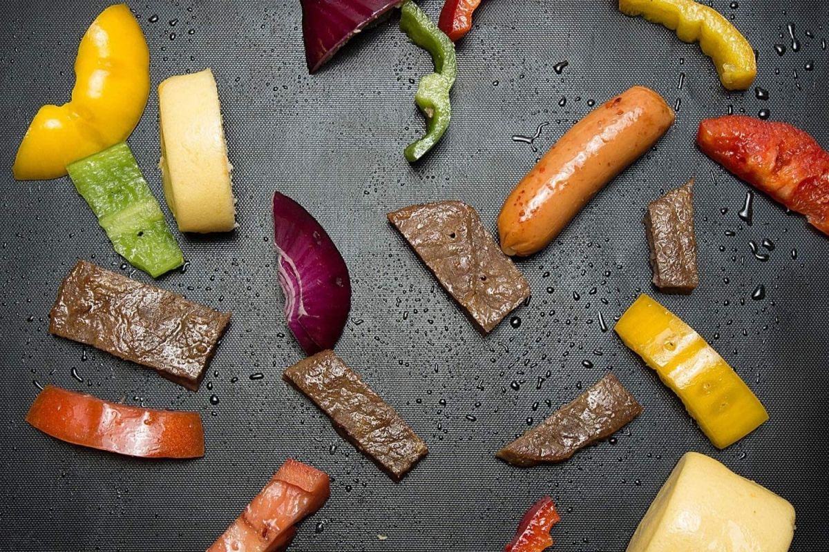 Chopped vegetables and sliced meat on top of the best grill mat during grilling.