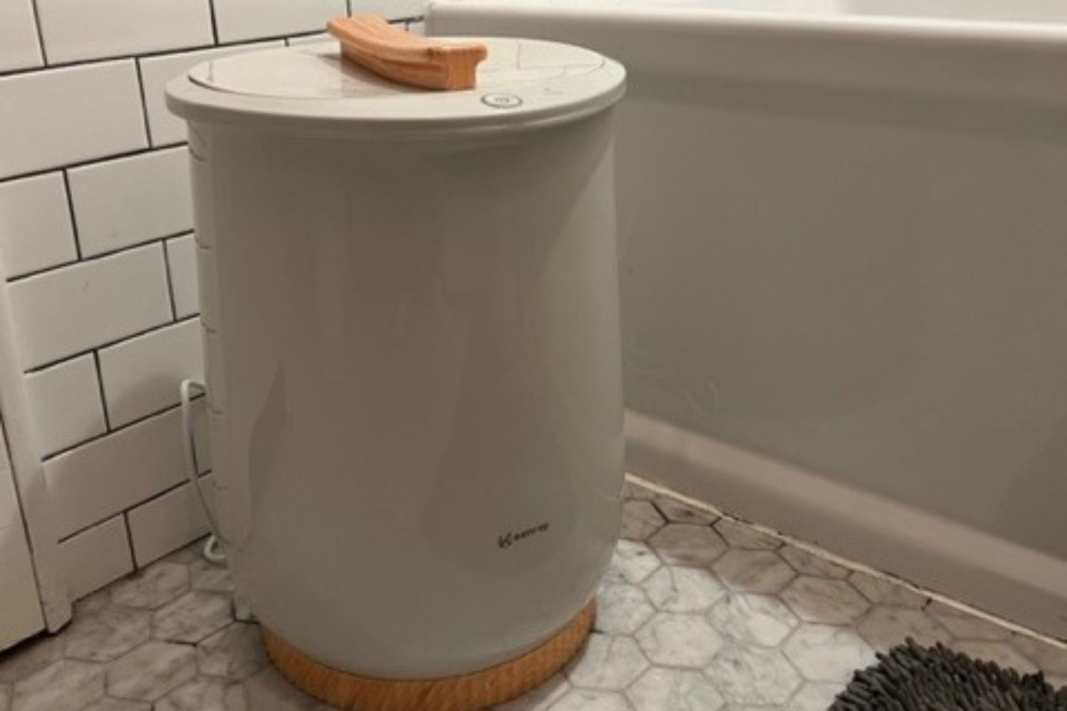 The The Keenray Bucket Towel Warmer on a tiled bathroom floor next to a bathtub.