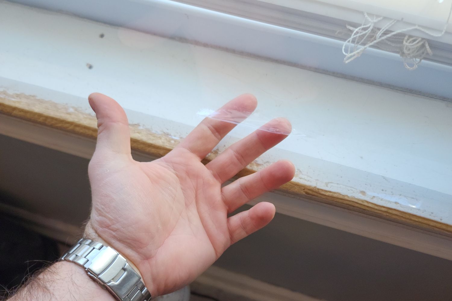 A person reaching their fingers under a layer of the best window insulation kit installed on a window.