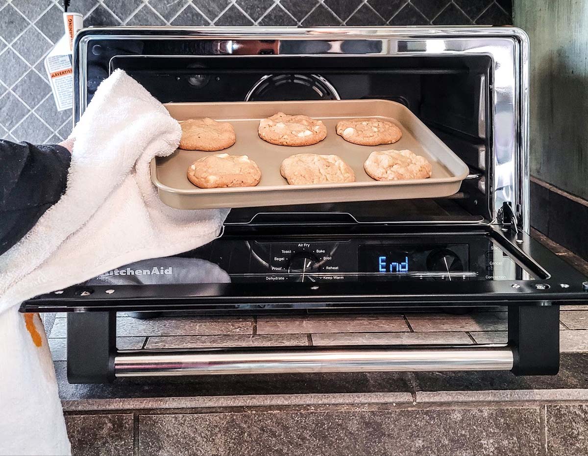 A person taking a tray of freshly baked white chocolate chip cookies out of the best air-fryer toaster during testing.