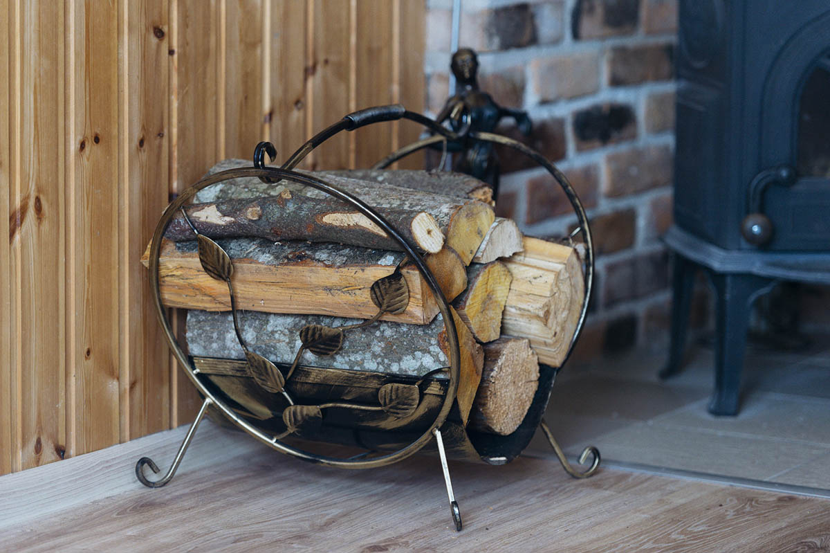 The best firewood rack option filled with firewood next to a wood-burning stove backed by a brick surround
