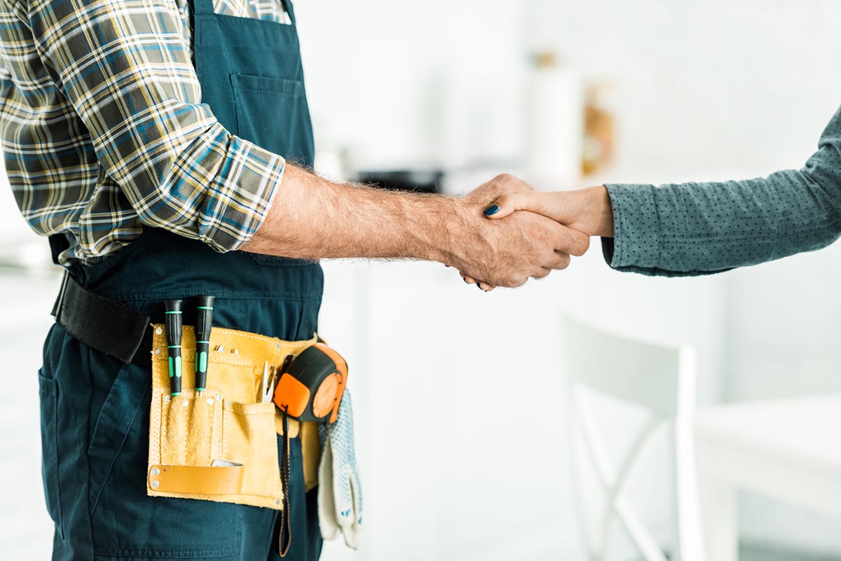 A close up of a handyman wearing a tool belt shaking someone's hand.