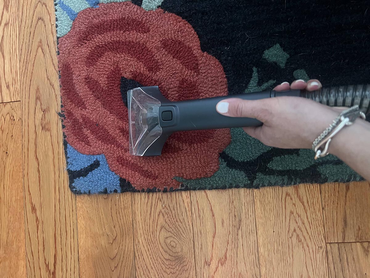 A person using the best portable carpet cleaner to spot clean a floral rug.