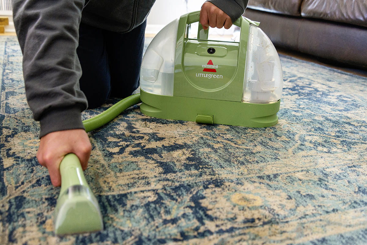 A person using the best portable carpet cleaner to spot clean a patterned rug.