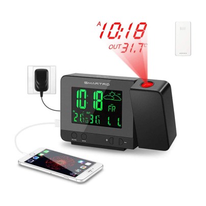 The Smartro SC31B Digital Projection Alarm Clock on a white background next to a phone plugged into the clock and an outlet, a remote, and an illustration of time projected above the clock.