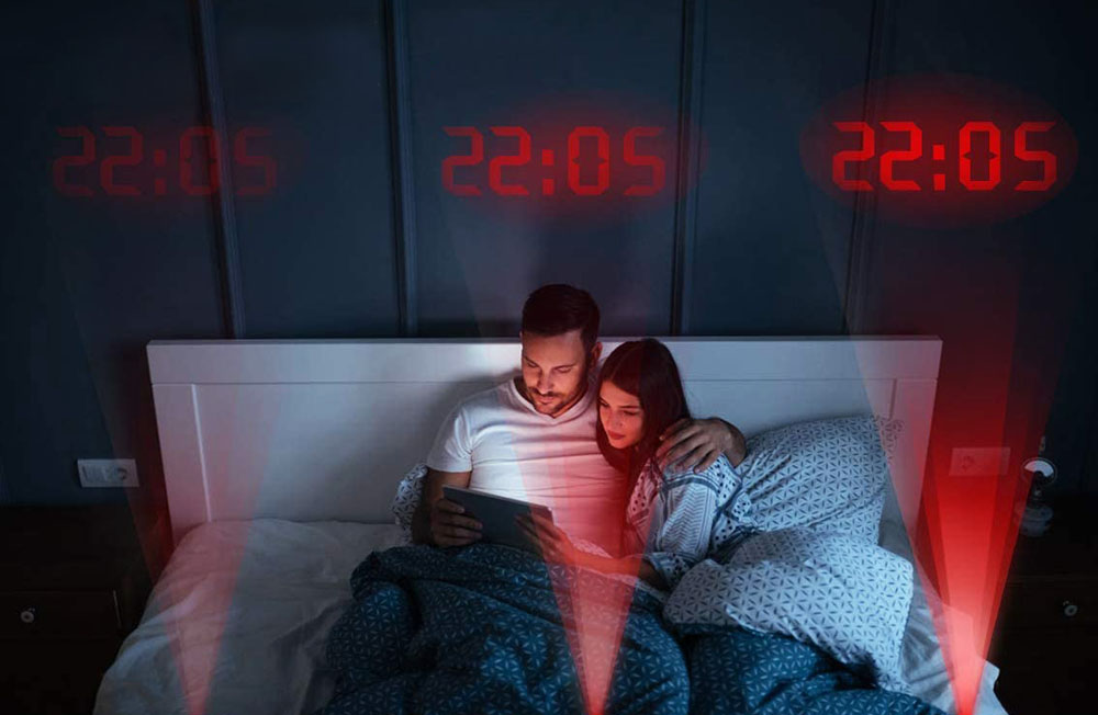 A couple cuddling in bed with multiple projections of 22:05 lighting the air above them.