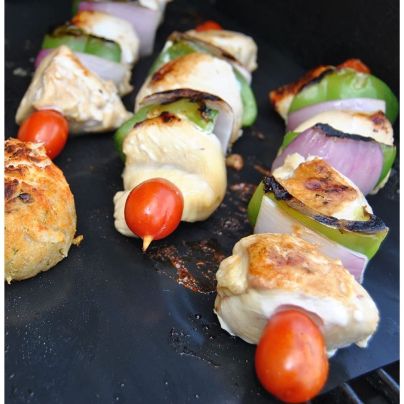 The Kona Best BBQ Heavy-Duty Grill Mats with a set of chicken and vegetable skewers cooking on them.