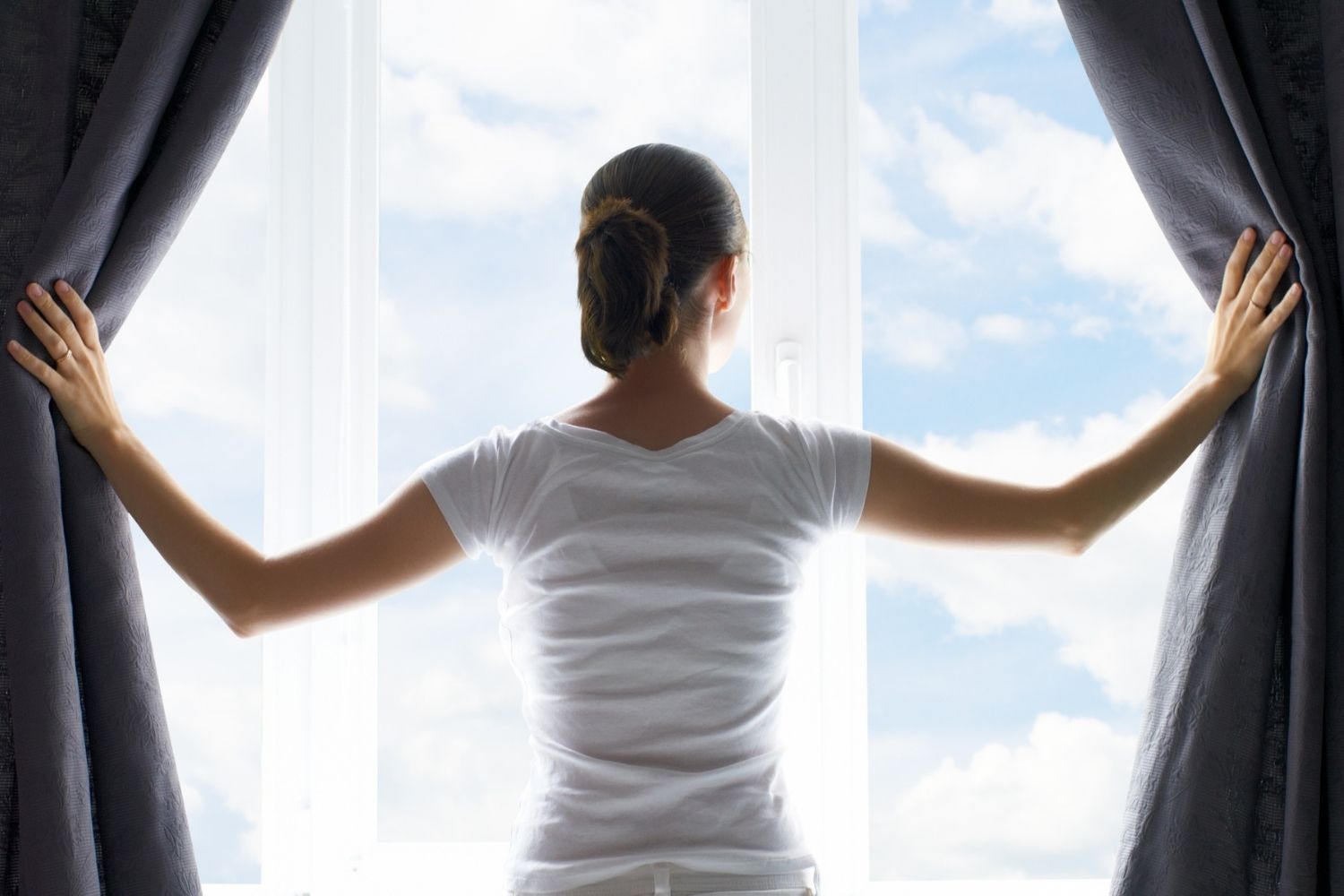 A woman parting the best soundproof curtains option to look out the window