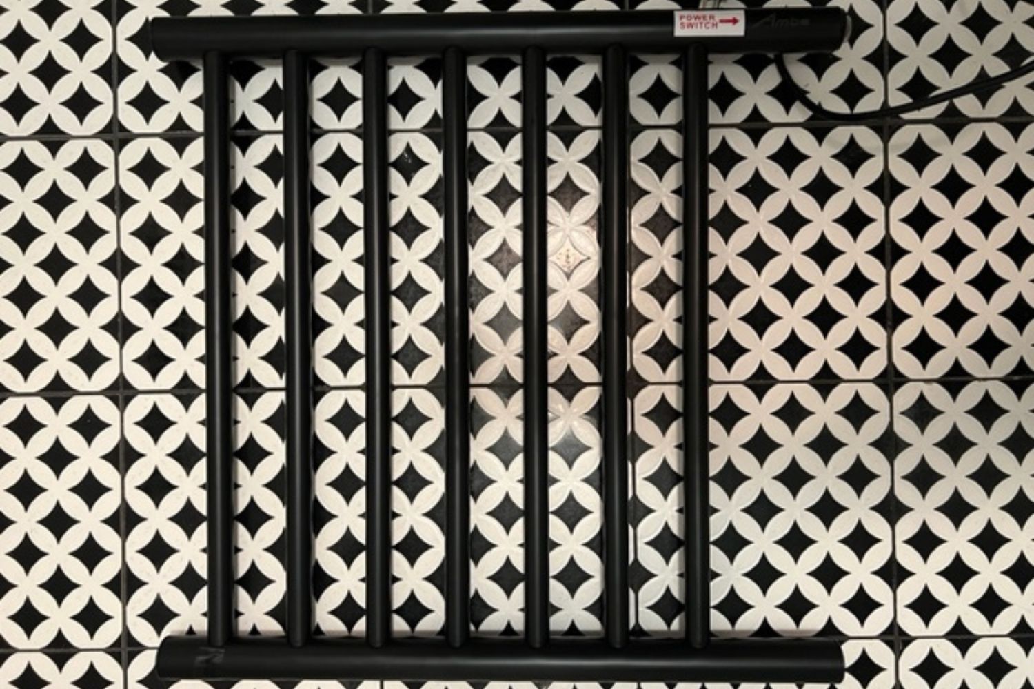 The Amba Radiant Small 7 Bar Towel Warmer on a black and white tiled floor before testing.