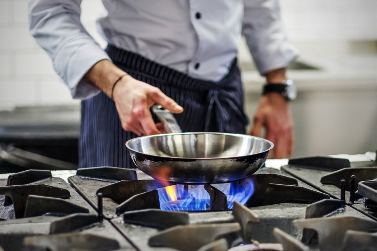 A chef warms a saute pan on the best gas cooktop option
