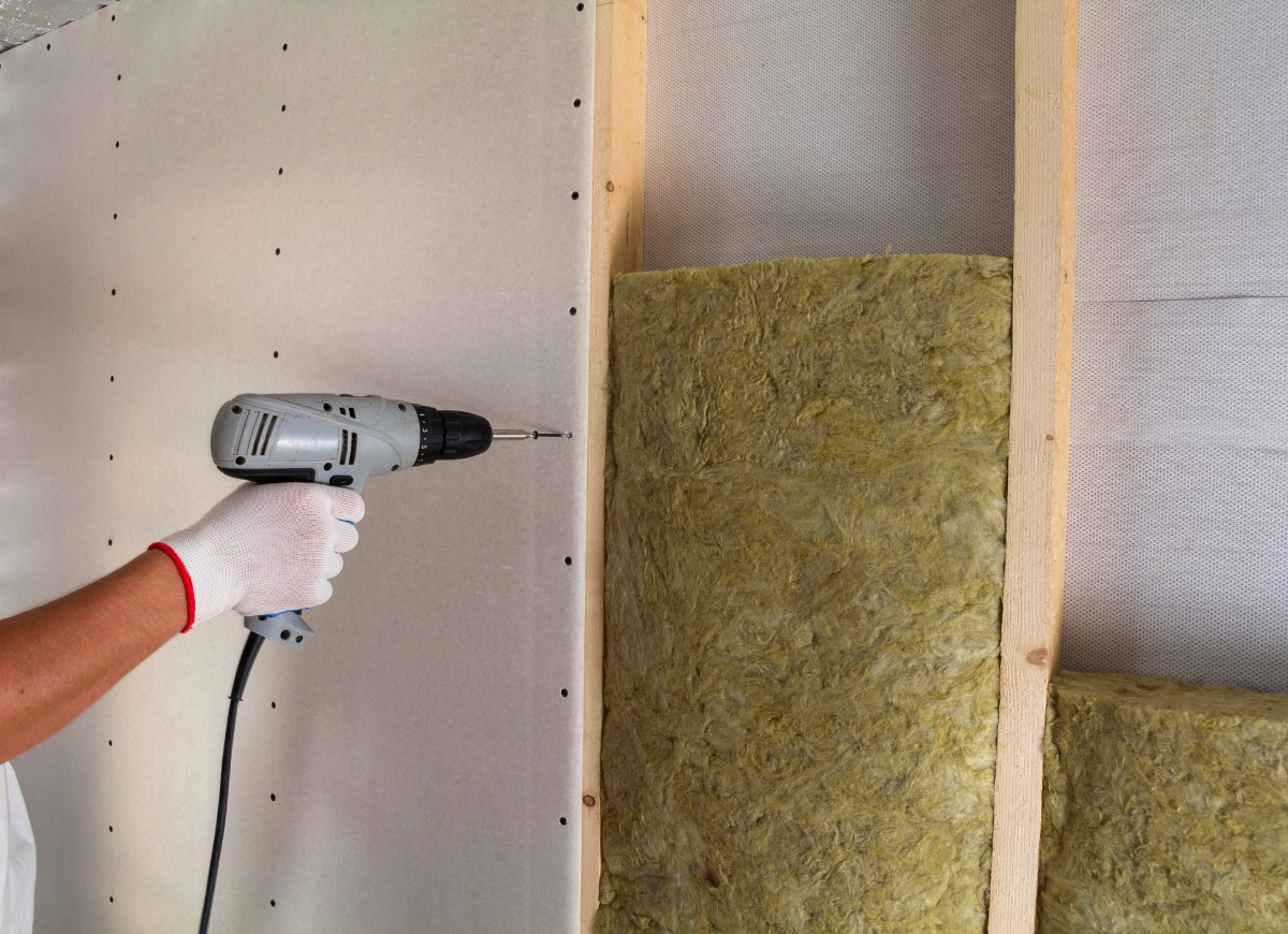 Close up of worker with electric screwdriver fastening drywall